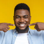 Black man smiles as he points to his teeth after professional teeth whitening