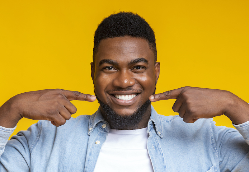 Black man smiles as he points to his teeth after professional teeth whitening