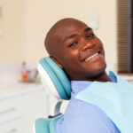 Black man smiling while sitting in a dental chair during his routine checkup at the dentist