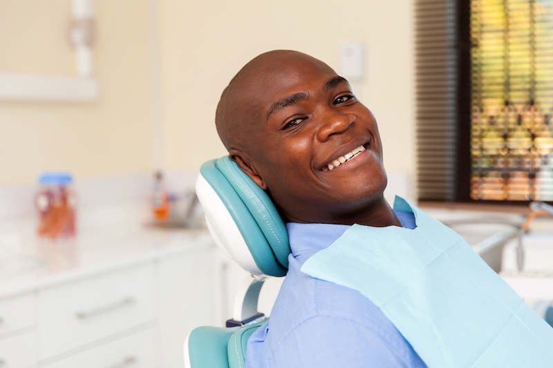 Black man smiling while sitting in a dental chair during his routine checkup at the dentist