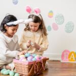 Two young girls wearing bunny ears go through their Easter eggs in a basket together