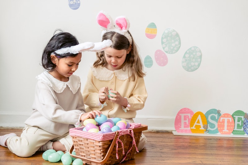 Two young girls wearing bunny ears go through their Easter eggs in a basket together