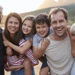 A multigenerational family of grandparents, parents, and children smile together outside