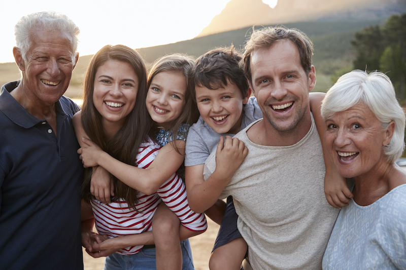 A multigenerational family of grandparents, parents, and children smile together outside