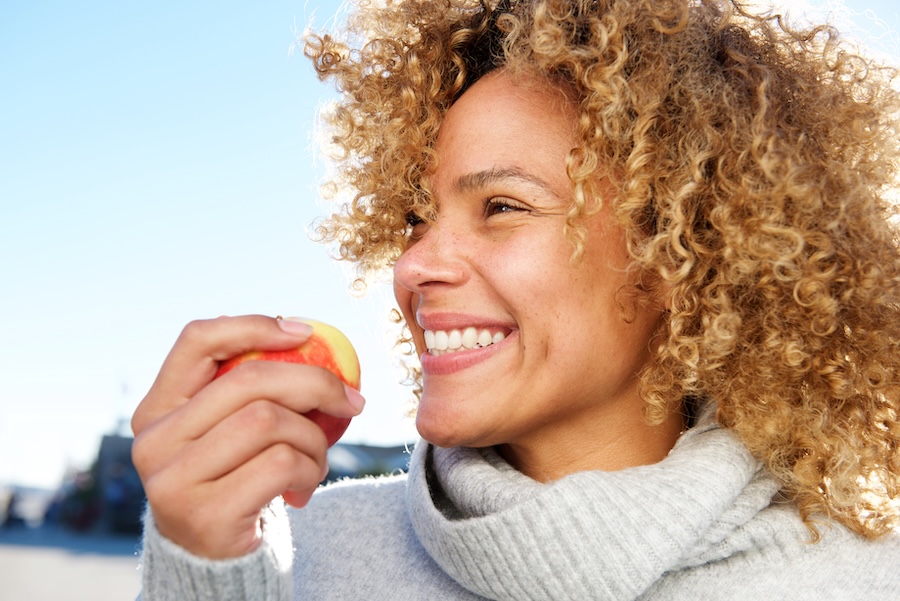 woman eating an apple, which is on the list of foods that clean teeth